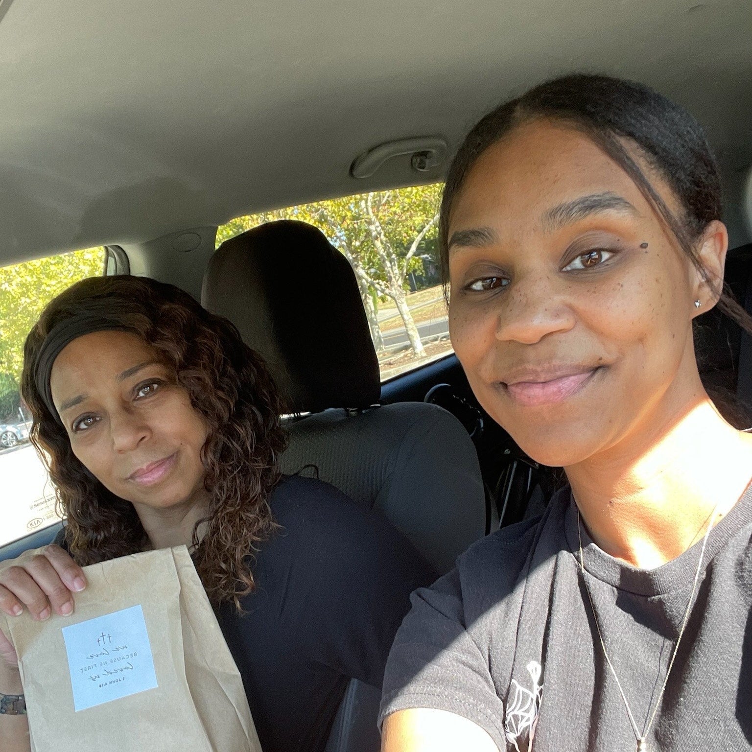 Two women sitting in a car, one holding a brown paper bag.